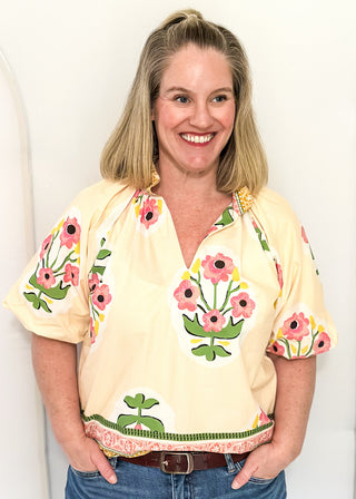 Women's short sleeve ecru top with pink floral bundles and decorative hem and collar. 