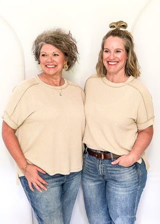Two women wearing matching beige tops and blue jeans standing against a white background