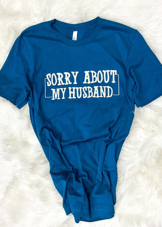 Blue t-shirt with 'Sorry About My Husband' text on a white fluffy surface