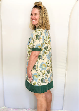 Short sleeve ecru dress with light blue and dark green blooms. Dark green contrast with Ivory stitching stripes on sleeves, hem, and v-neck collar.  