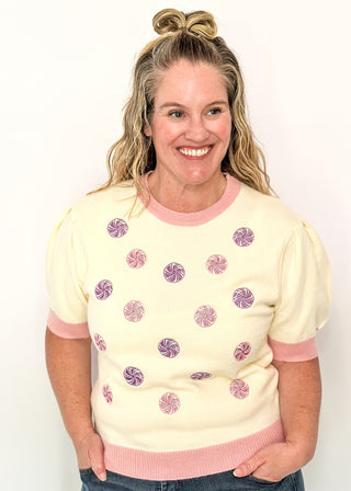 Cream short sleeve sweater with puff sleeves, pink trim, and sequin peppermint candy accents on the front
