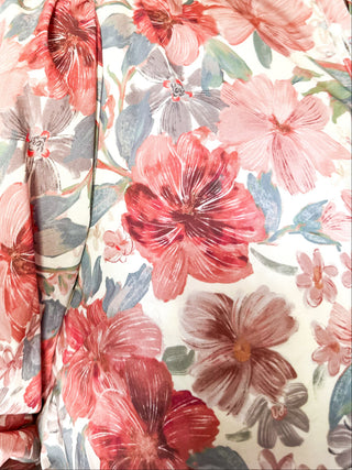 A close-up of a person wearing a floral blouse with red, pink, and gray flowers on a cream background, photographed indoors with a ceiling fan and room visible in the background.