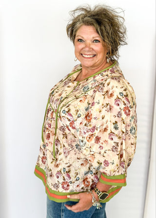 Soft floral Babydoll top with 3/4 puff sleeve, orange and green strip detail on banding of hem and sleeve. green ribbon detail on the front and tie at the collar. 