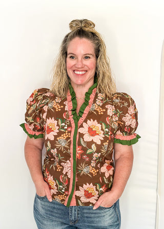 pink and golden botanicals on a brown background.  Short ruffle sleeves, v-neck ruffle collar in pink and green 