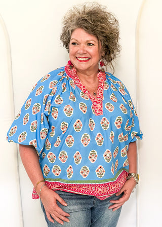 Bright blue 3/4 sleeve top with floral pattern, smocked collar with matching coral floral neckline and hem. 