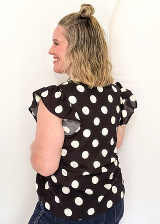 Women's black blouse with cream polka dots, striped split neckline, and flutter sleeves.