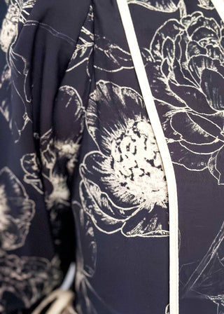 close up of black midi dress with cream piping and tie details on sleeves and waist.