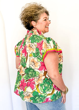 Bright floral blouse in pink, green, and yellow tones with split neckline and cap sleeves.
