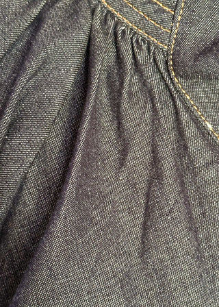 Close up of women's indigo denim-look blouse featuring a smocked split neckline, puff sleeves, and a relaxed fit.
