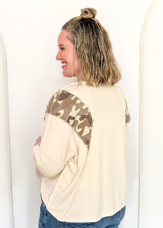Cream knit colorblock top with camo print shoulder panels, ribbed taupe sleeves and cuffs, and a crew neckline.