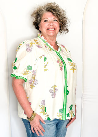 off white floral short sleeve button front blouse with pink and green flowers, featuring puff sleeves, ruffled neckline, and green trim.
