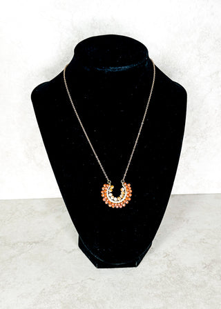 Necklace with a brownish beaded circular pendant on a black bust against a white background