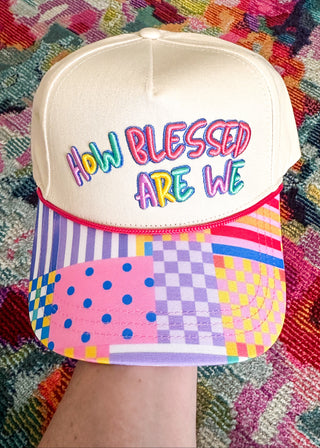 snap back hat with multicolored patchwork brim featuring polka dots, stripes, checkerboard patterns in pink, purple, blue, and yellow. Embroidered "How Blessed Are We" on the front. 