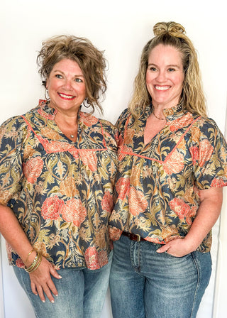 Short puff sleeve navy floral top. Florals are terracotta and coral.  V-neck with coral piping detail on chest.