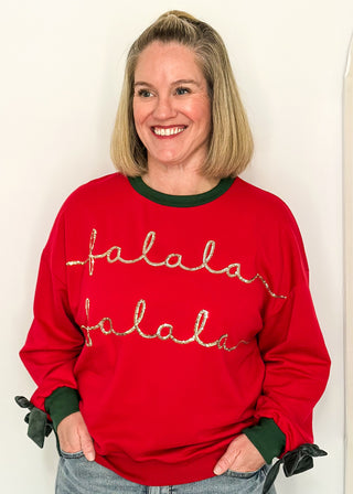 woman wearing a red long sleeve top with Hunter Green contrast, velvet bows on sleeve and sequin lettering "fa La La La la"