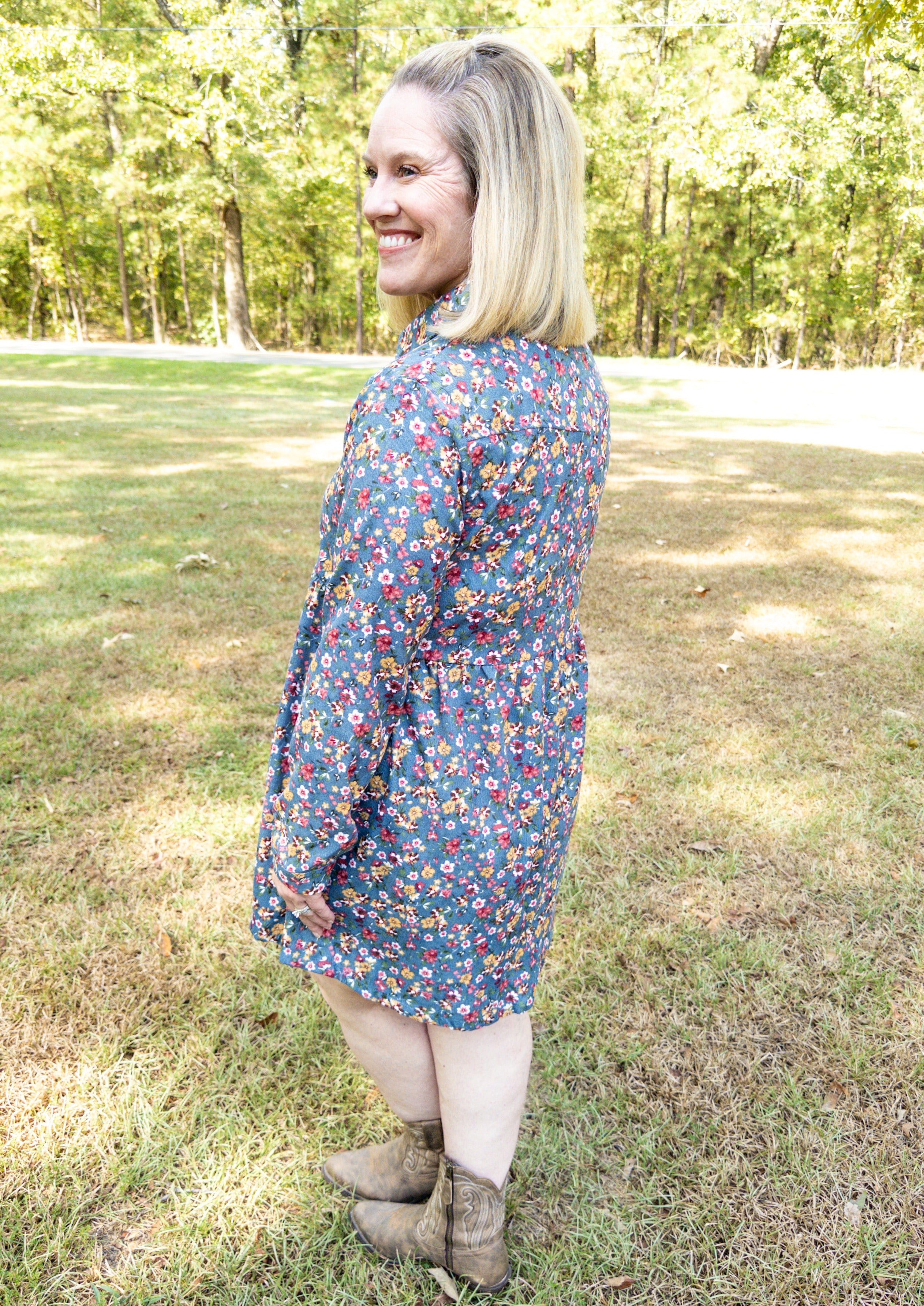 side/back view of Dusty blue corduroy dress with long sleeves and a soft colored floral pattern all over. The dress has buttons all down the front and a collar.