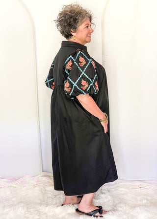 Women wearing a black midi dress with embroidered puff sleeves and a smocked bodice