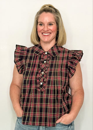 woman wearing a dark navy plaid top with flutter sleeves and rhinestone buttons.