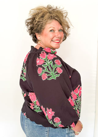 Woman wearing a dark blouse with floral embroidery against a white background