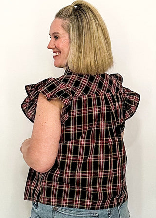side view of woman wearing a dark navy plaid top with flutter sleeves 