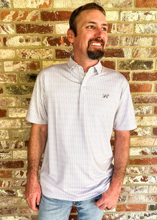 A man wearing a short-sleeve button-down polo shirt with a small embroidered bird logo on the chest, standing in front of a brick wall.