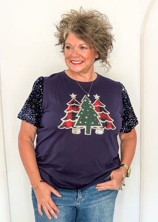 woman wearing a navy short sequin sleeve top with plaid and green embellished trees