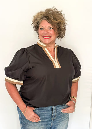 Woman wearing a black blouse with white trim and blue jeans against a white background