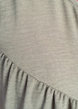 Close up of charcoal gray sleeveless woven jumpsuit with ribbon tie neckline, pockets, and flowy wide-leg fit.
