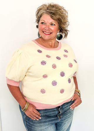 Cream short sleeve sweater with puff sleeves, pink trim, and sequin peppermint candy accents on the front
