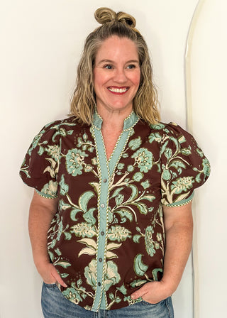 woman standing in a brown, cool blue and cream button up top and jeans.
