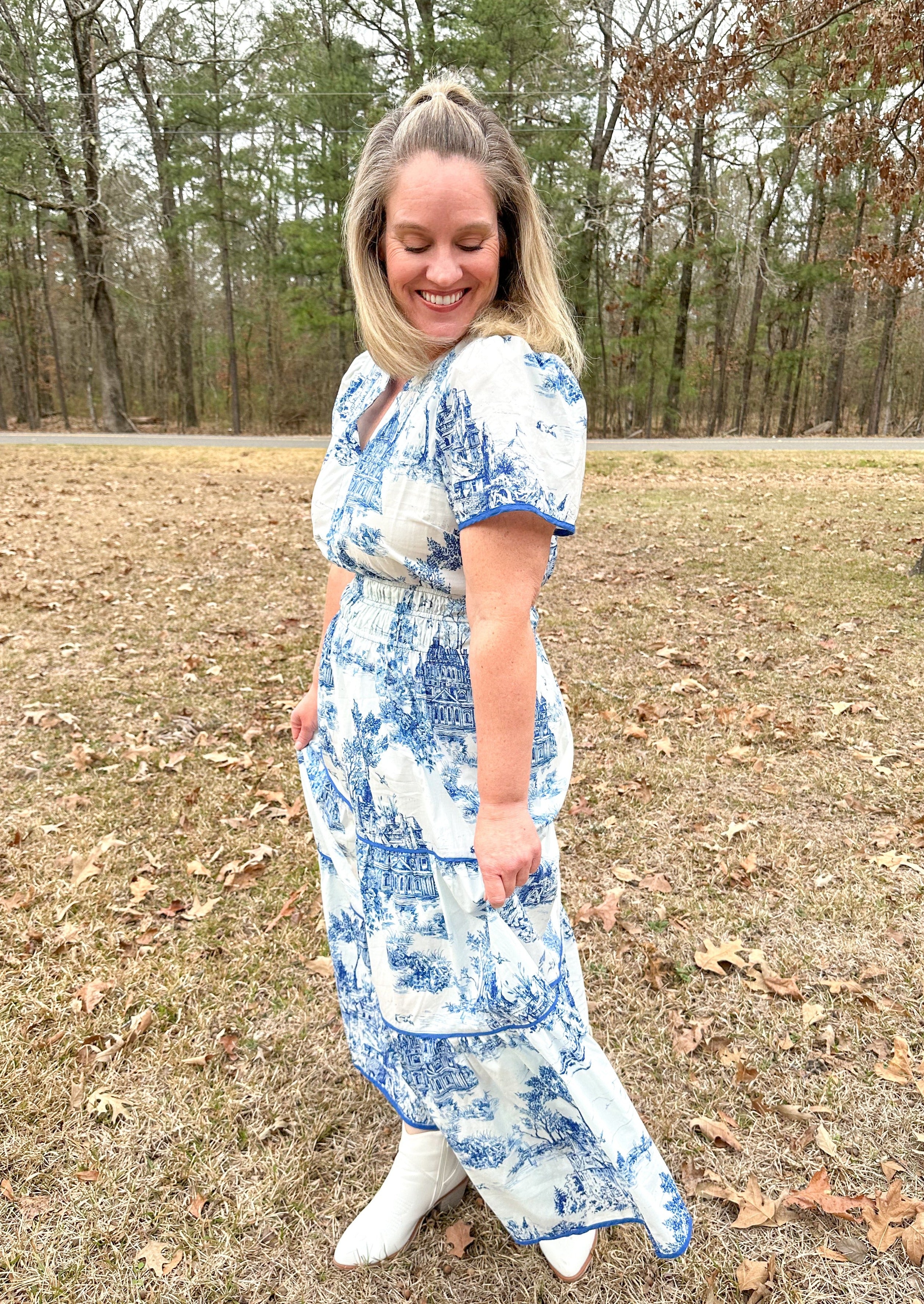 Blue landscape print on white maxi dress, blue trim detail around tiers and cuffs, slight v-neck, elastic banded waist