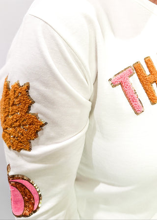 Light Ivory Long sleeve top with terracotta leaves and pink pumpkin patches sewn on the sleeves. "Thankful" chenille patches across the chest in pink and terracotta. 
