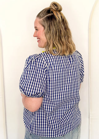 Women’s gingham blouse with decorative buttons and statement neckline detail.