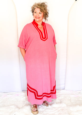 Pink midi-length dress with contrast red trim at neckline and hem, short sleeves with elastic, relaxed fit, and pockets.