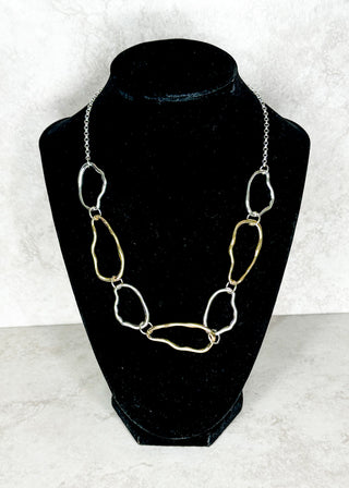 Gold and silver necklace on a black velvet bust against a white background
