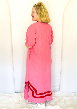 Pink midi-length dress with contrast red trim at neckline and hem, short sleeves with elastic, relaxed fit, and pockets.