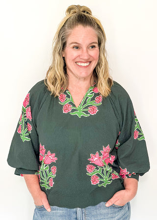 Woman wearing a green blouse with floral embroidered print against a white background