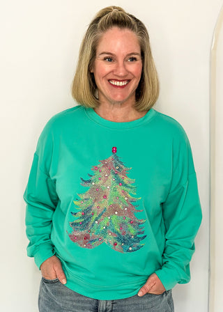 woman wearing a long sleeve top in aqua with watercolor tree graphic and gemstone details.