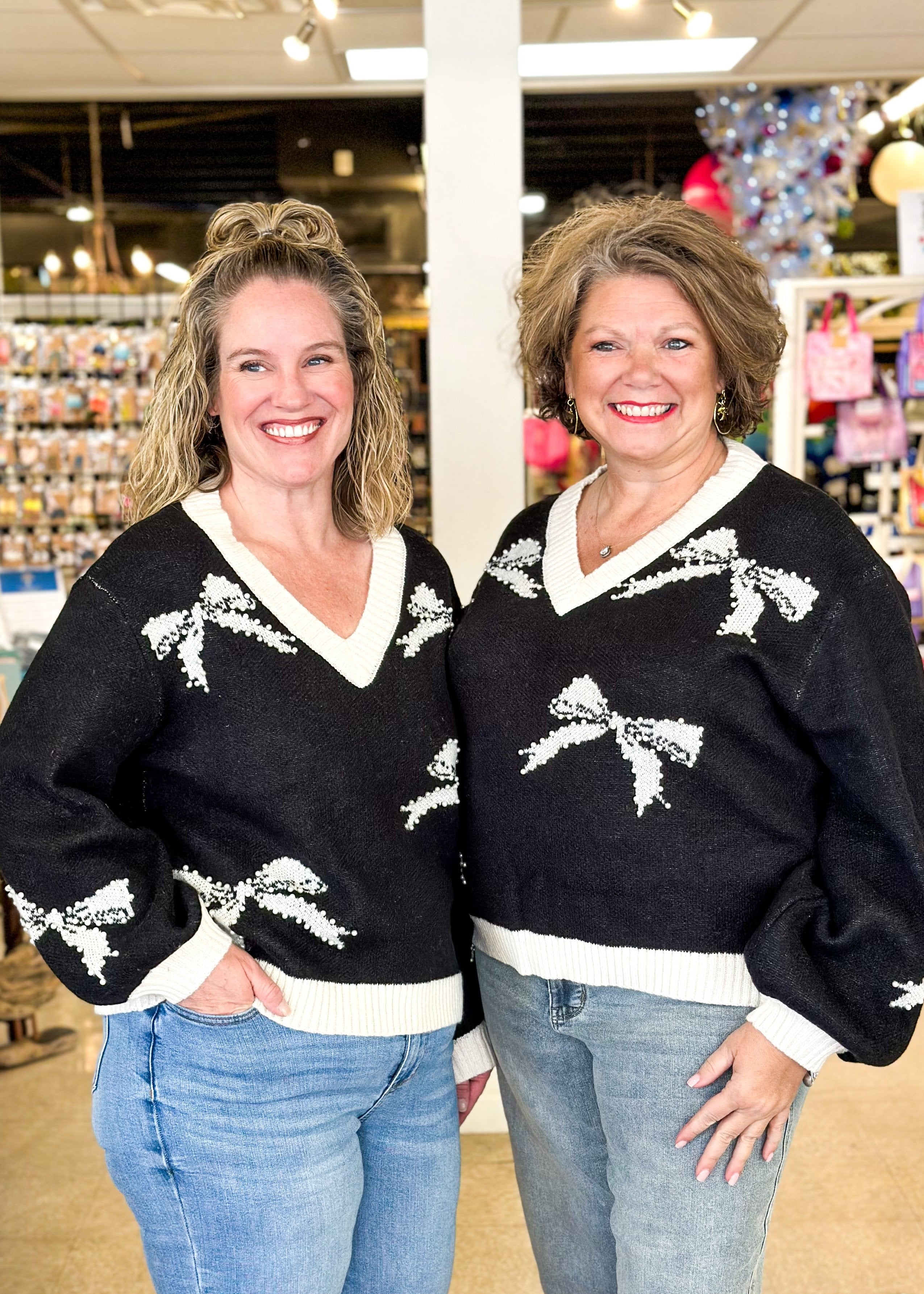 black v-neck long sleeve sweater with cream bands around neck, cuff and hem, cream bows outlined in pearls on sweater