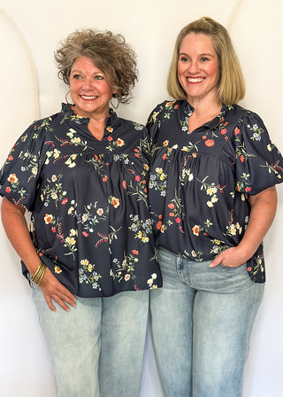 two women standing in a Navy top with floral print.