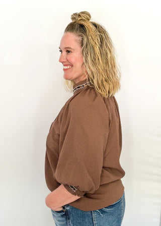 Chocolate brown v-neck top with 3/4 length sleeve, leopard lace detail around sleeve, collar, and v-neck.