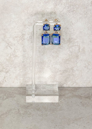Blue gemstone dangle earrings displayed on a stand.