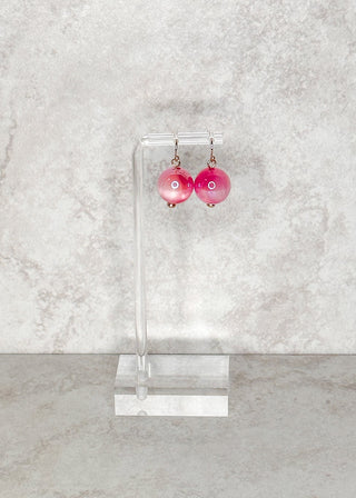 Pink bead fish hook earrings on a clear stand against a light gray marble background