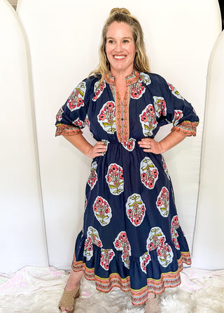 Navy maxi dress with colorful floral medallion print, orange embroidered trim at neckline, and smocked cuffs