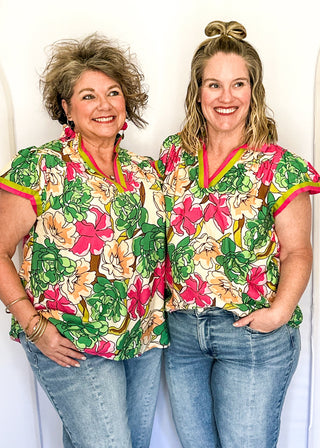 Bright floral blouse in pink, green, and yellow tones with split neckline and cap sleeves.