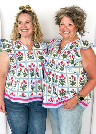 Flutter sleeve top with off white background and soft blue grid pattern-large magenta florals with green stems/leaves in each grid.  Soft blue ribbon trim on sleeve and collar.  Soft blue ribbon tie neck.  Soft blue and magenta trim on bottom band. 