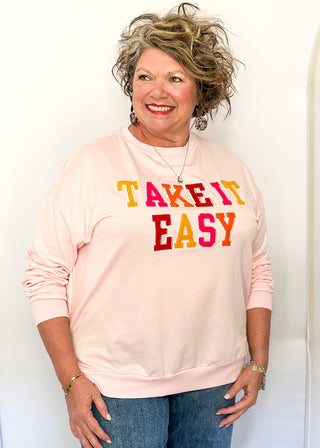 Lightweight pink long-sleeve top with multicolor chenille patch letters spelling “TAKE IT EASY”
