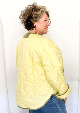 Light sage green quilted jacket with darker contrast trim, long sleeves, patch pockets, and button-front closure