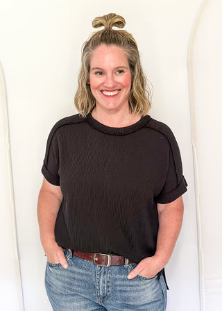 Woman wearing a black top and blue jeans standing against a white background