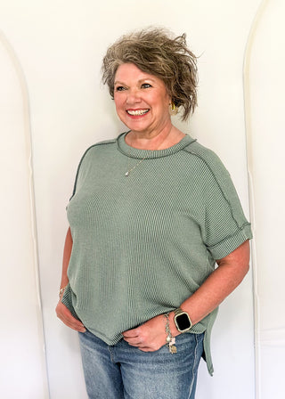 Woman wearing a green ribbed sweater and blue jeans against a white background